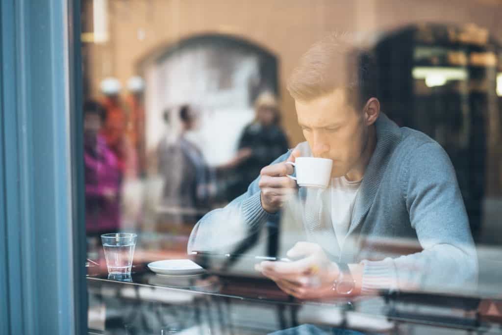  a man drinking coffee in a coffee shop and looking at his tablet 