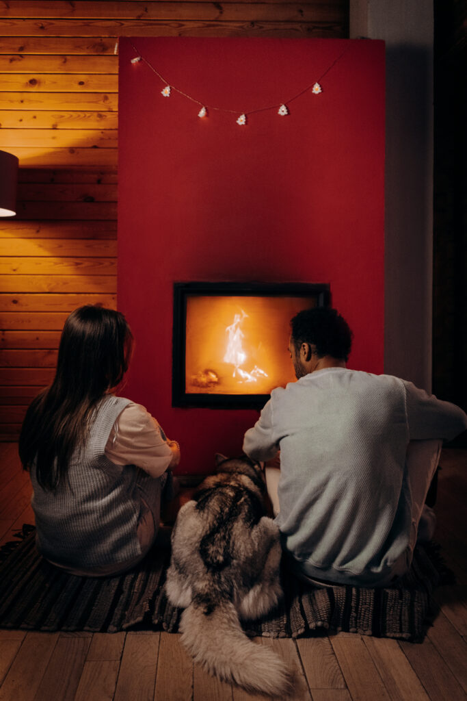 two people and a dog sit in front of a fire place 
